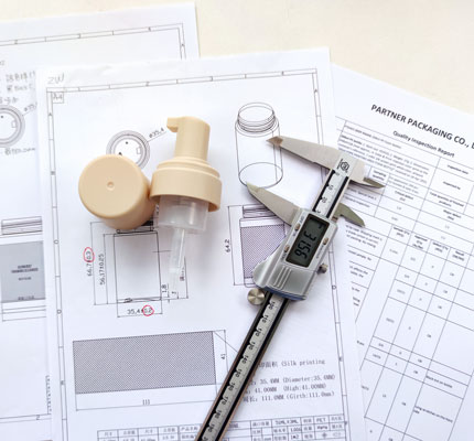 Foam pump with caliper on desk over technical drawings.